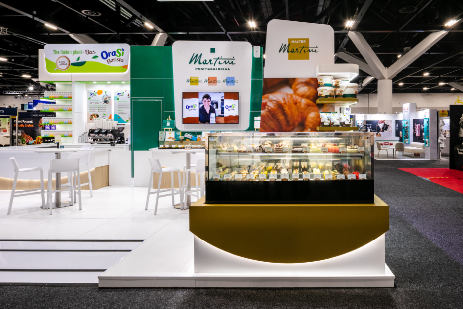 Custom built exhibition demonstration counter with full-height green feature wall panels, glass sneeze guard, and integrated shelving for Martini Professional at Restaurant & Foodservice Show Australia 2026