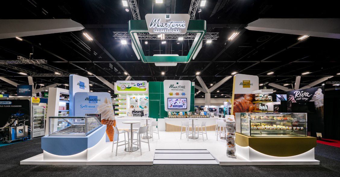 Large-format custom island exhibition stand with suspended hanging sign, multiple branded display zones, and illuminated platform flooring built for Martini Professional at Restaurant & Foodservice Show Australia 2026