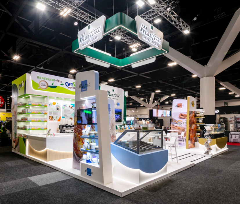 Bespoke exhibition barista service counter with curved illuminated timber base, integrated green-lit product shelving wall, and espresso bar built for Martini Professional at Restaurant & Foodservice Show Australia 2026