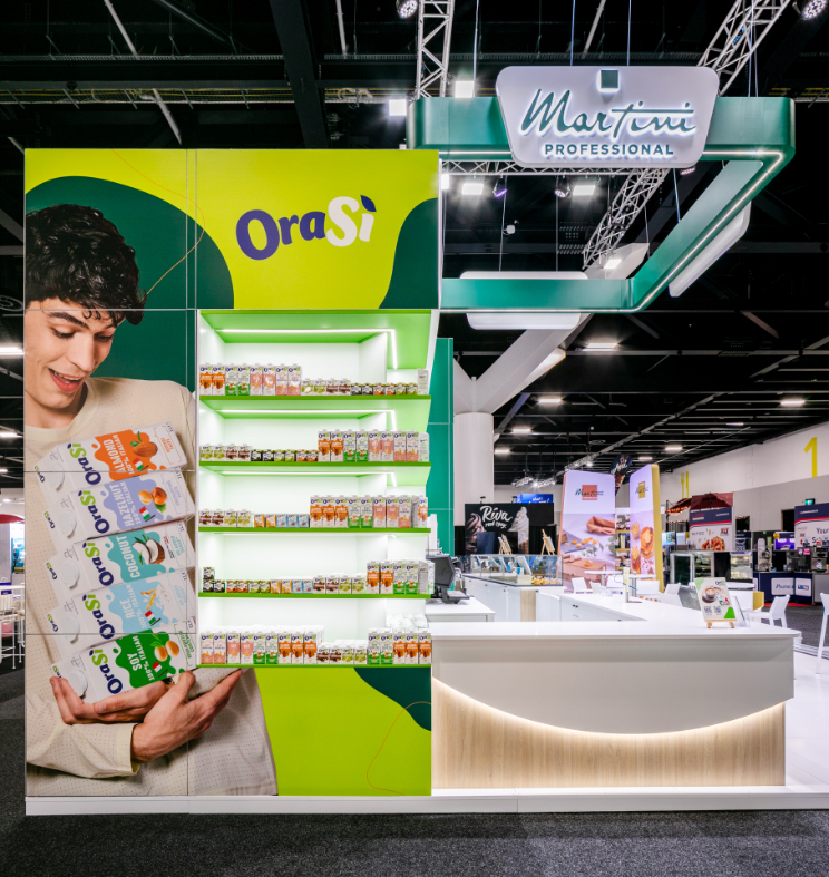 Custom exhibition stand panoramic view with large-format OraSì display wall, illuminated product shelving, and curved timber-base service counter built for Martini Professional at Restaurant & Foodservice Show Australia 2026