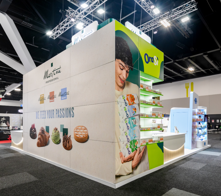 Custom exhibition stand corner build with large-scale graphic wall panel, bespoke illuminated product shelving, and green feature wall for Martini Professional at Restaurant & Foodservice Show Australia 2026